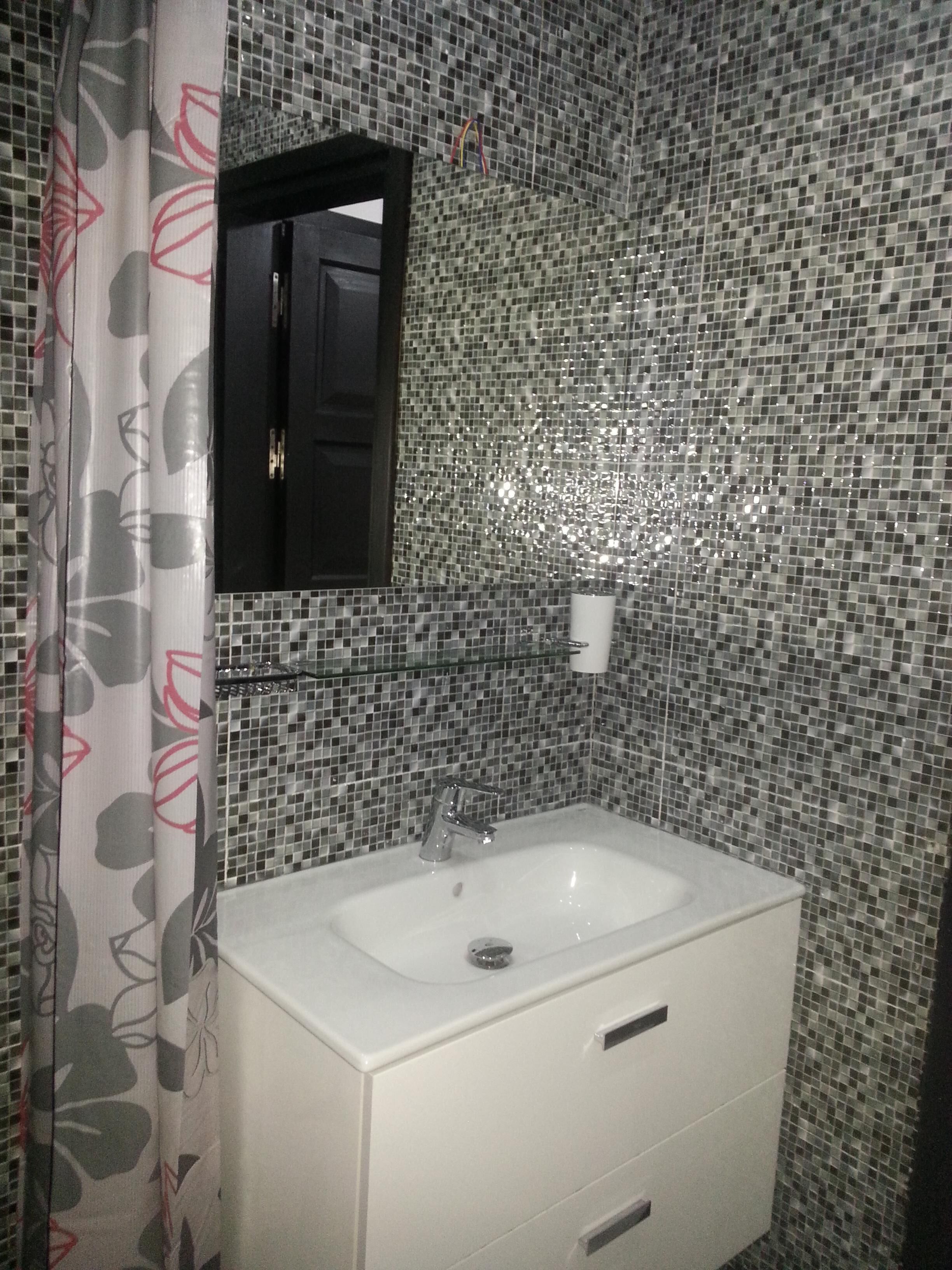 Une salle de bain avec un lavabo blanc, un miroir au-dessus et un mur recouvert de carreaux.