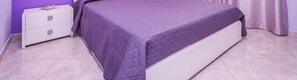 A bed with a quilted cover, a white nightstand, and a purple wall.