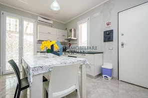 A kitchen with white cabinets, a dining table with a patterned tablecloth, and a trash bin.
