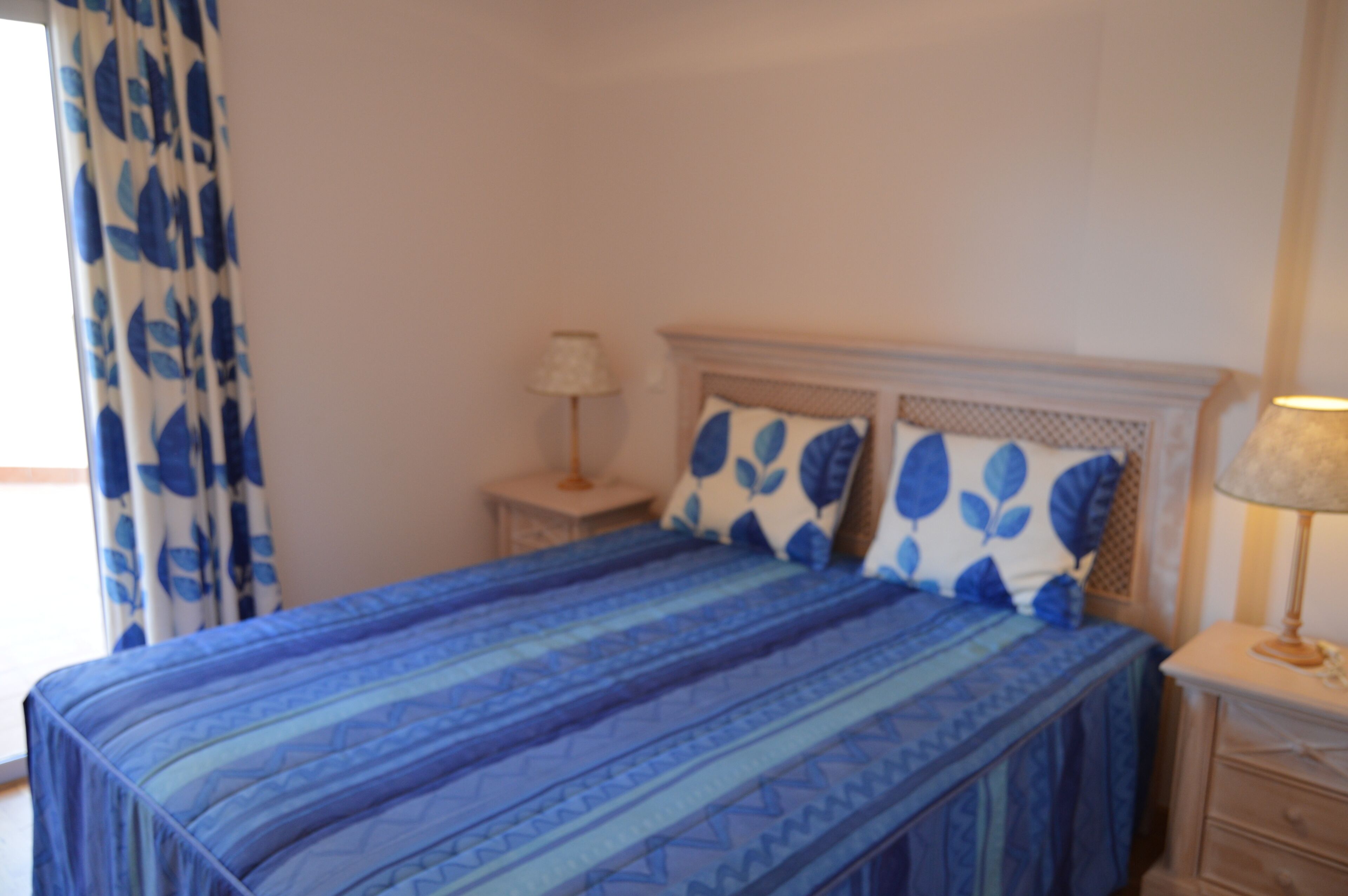 Una camera da letto con un letto, un comodino, una lampada e una finestra con tende.