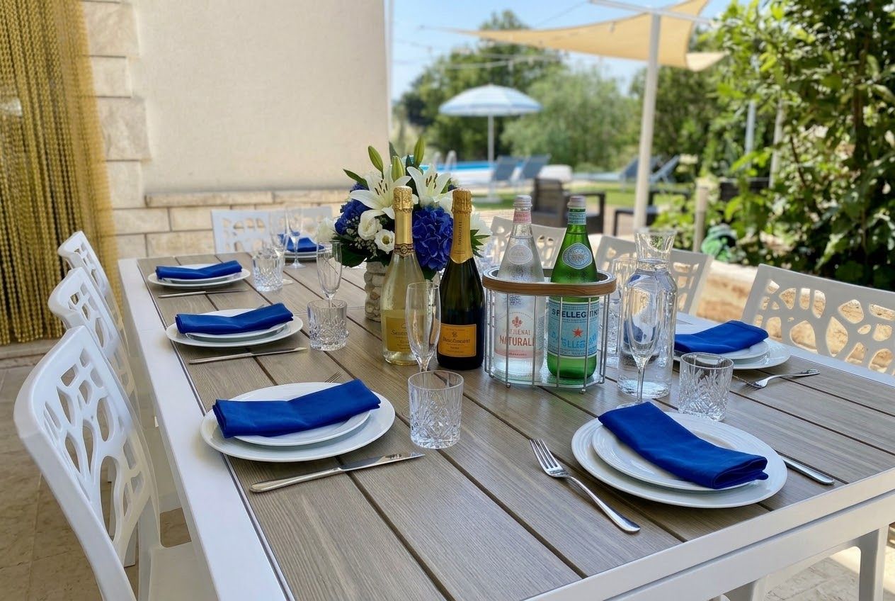 An outdoor dining table set with plates, napkins, cutlery, and bottles of wine.