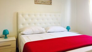 Un lit bien fait, avec une couverture rouge, des oreillers blancs et une tête de lit blanche.