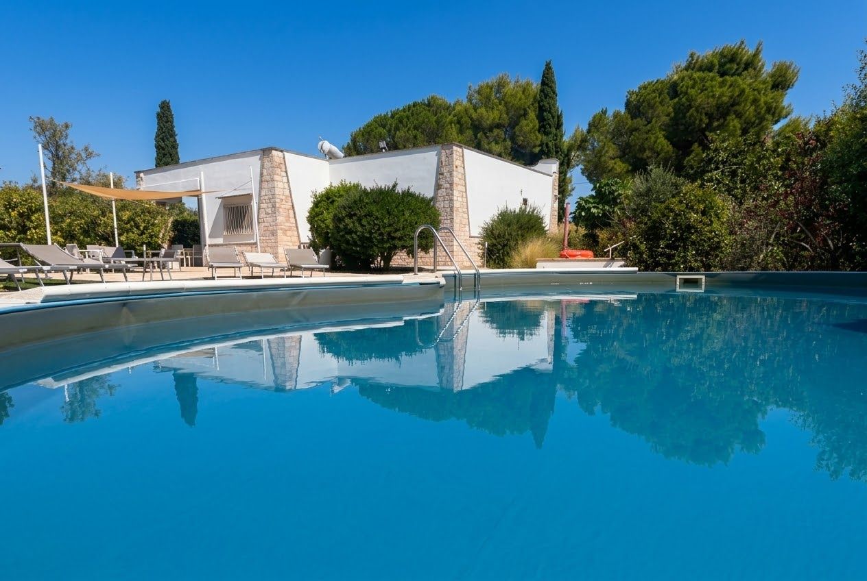 Una piscina con sillones de descanso y un edificio de paredes de piedra y blanco.