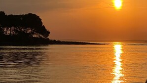 Un coucher de soleil sur une étendue d’eau calme, avec la silhouette d’arbres sur la gauche.