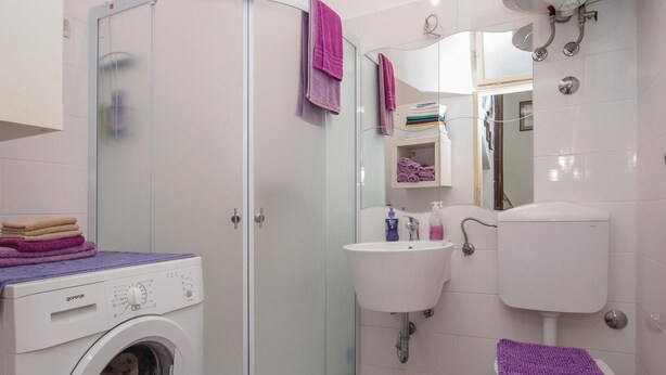 Un baño con lavadora, lavamanos, inodoro y cabina de ducha de vidrio.