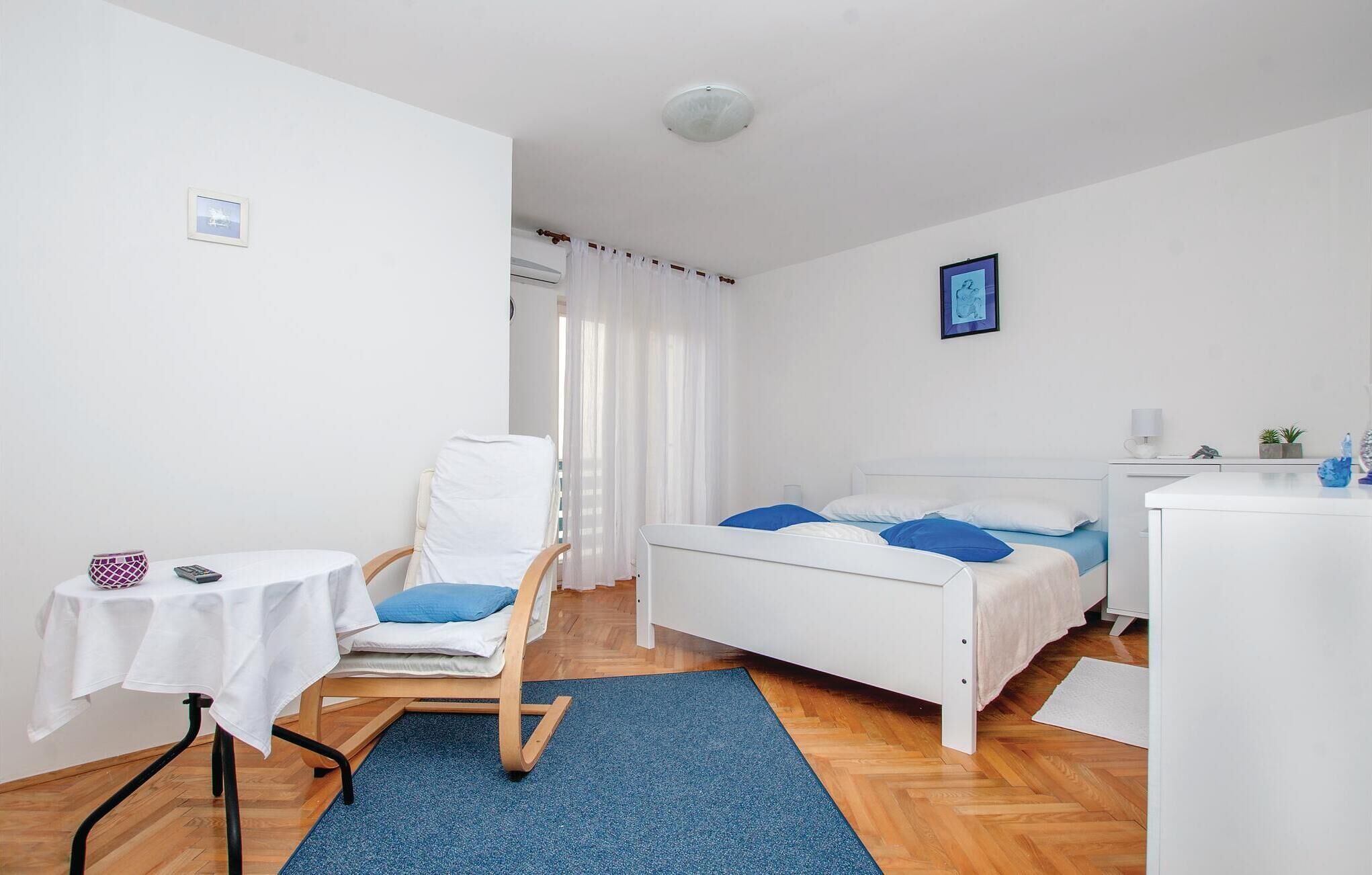 A bedroom with a bed, a chair, a small table, and a desk.