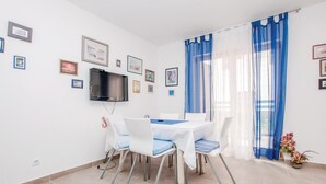 Una zona de menjador amb una taula preparada per a quatre, un televisió de pantalla plana penjada a la paret i una finestra amb cortines blaves.