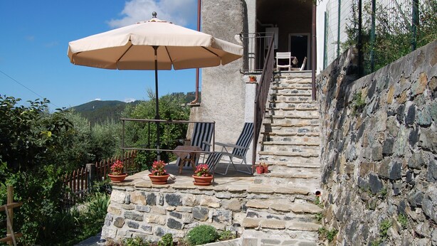 Eine Steintreppe führt zu einem Balkon mit Tisch, Stühlen, Sonnenschirm und Blumentöpfen.