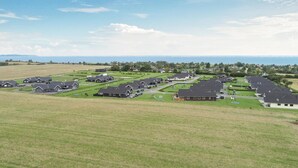 Zona residencial con casas alineadas, céspedes verdes y vista al mar en el fondo.