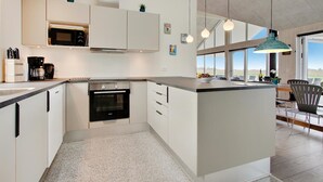 Una cocina moderna con horno empotrado, microondas y cafetera. Dos lámparas colgantes iluminan la isla.