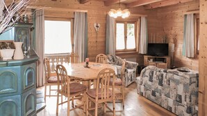 Et hyggeligt interiør i en hytte med et træbord, stole, en stribet sofa, et fjernsyn og et skab med pynteting.