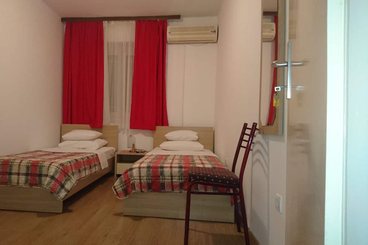 A small, well-lit bedroom with two single beds, a wooden floor, a red chair, and a mirror on the wall.