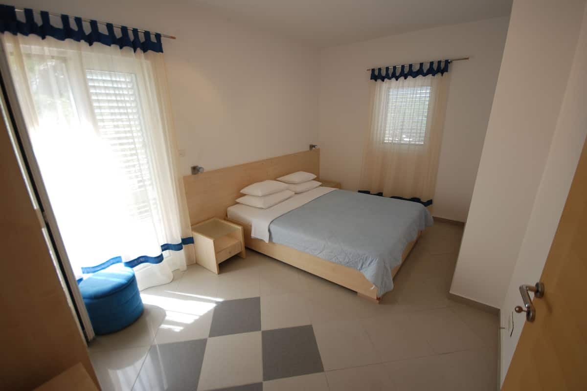 A bedroom with a bed, a bedside table, a small bench, and a window with curtains.