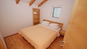 A bedroom with a bed, wooden floor, built-in shelving, and a window with blinds. - Springs apartments (Pržno)