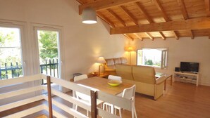 A spacious living area with a wooden ceiling, a sofa, a dining table, and a TV stand. - Sunny garden apartment in a breathtaking location (Saint-Pée-sur-Nivelle)