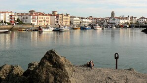A harbor with boats, a rocky shore, and buildings in the background. - Sunny garden apartment in a breathtaking location (Saint-Pée-sur-Nivelle)