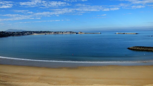 A coastal view with a sandy beach, calm sea, and a distant town with buildings and a lighthouse. - Sunny garden apartment in a breathtaking location (Saint-Pée-sur-Nivelle)