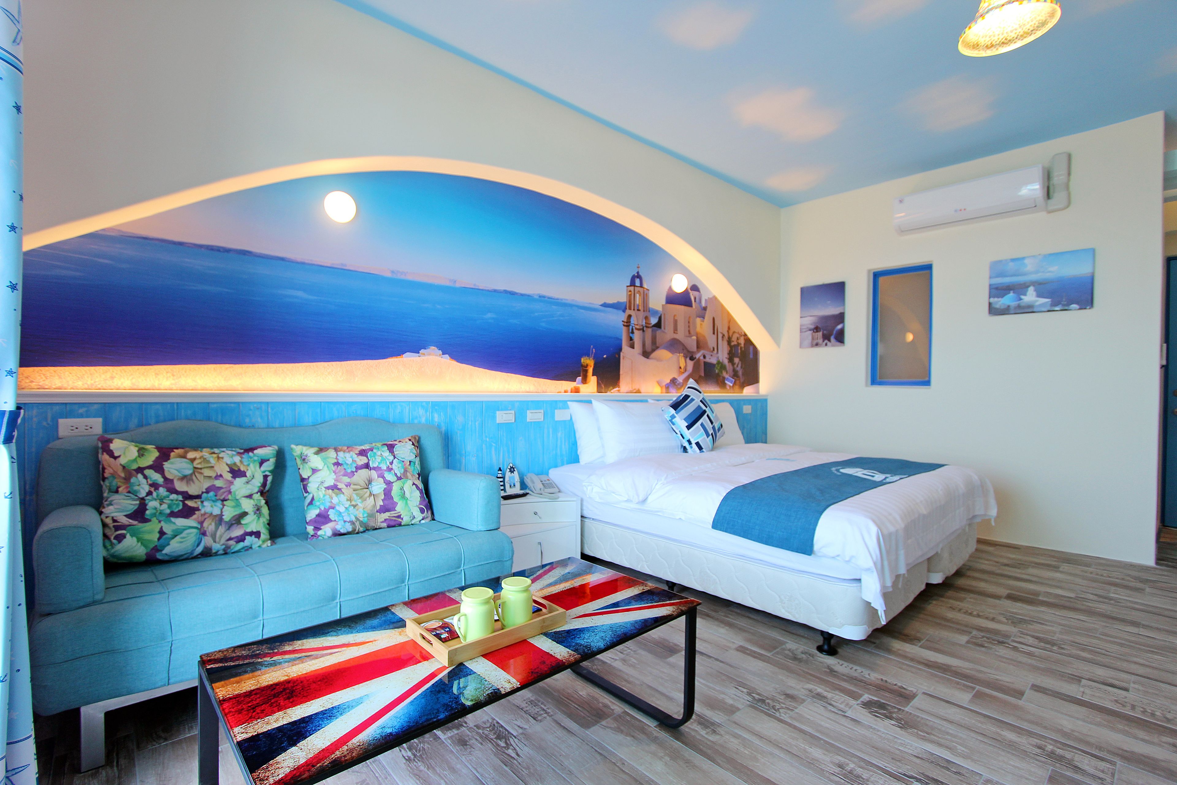 Una habitación con cama, sofá, una mesita de centro y un mural con una escena costera.