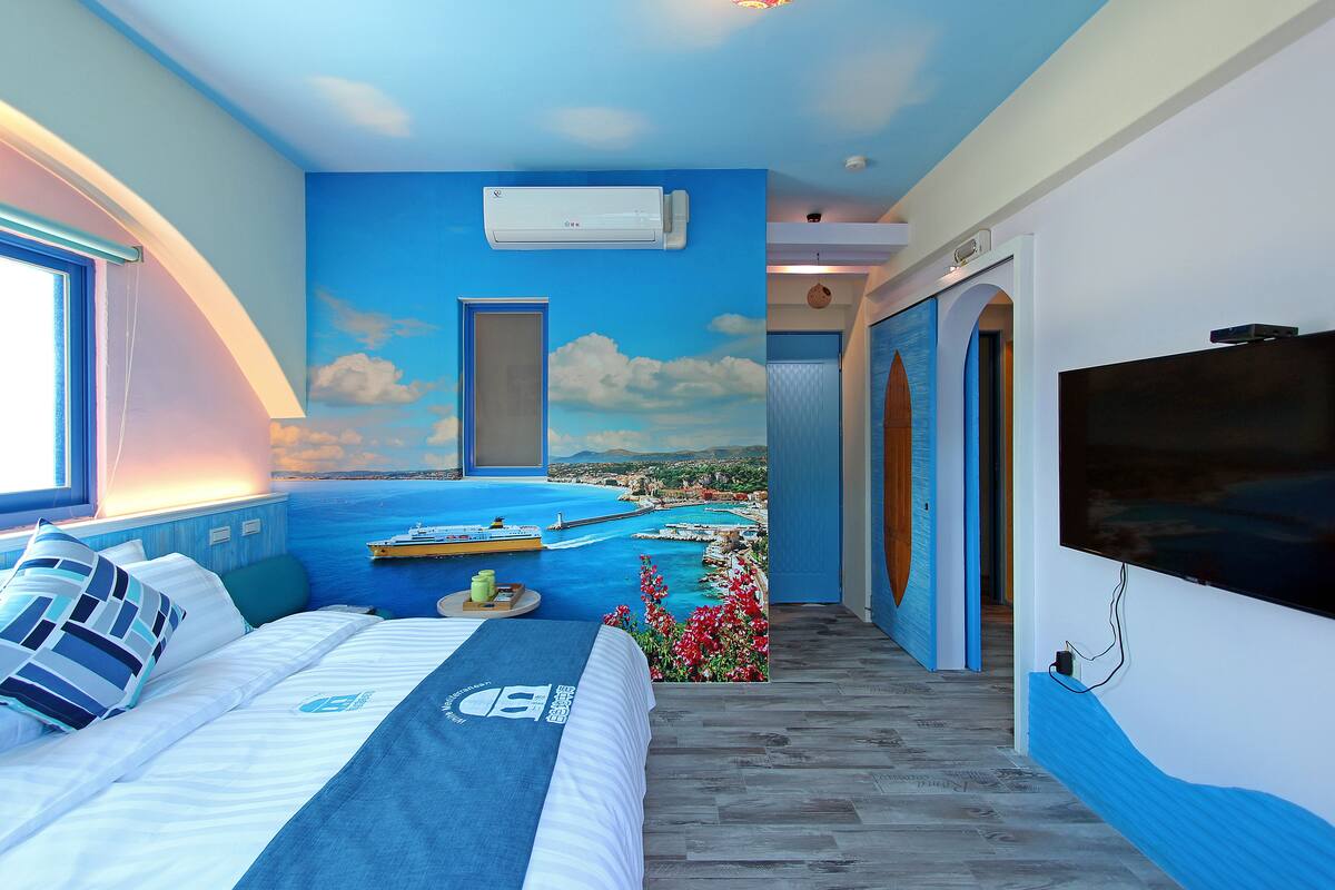 A bedroom with a large bed, a TV, and a mural of a coastal scene.