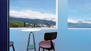 A room with a view of mountains and a cityscape through a large window. There is a round table with a chair and another chair with a green seat. - White Mediterranean (Hualien City)