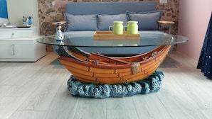 A room with a glass-top table featuring a boat-shaped base, a sofa with cushions, and a stone-patterned wall. - White Mediterranean (Hualien City)