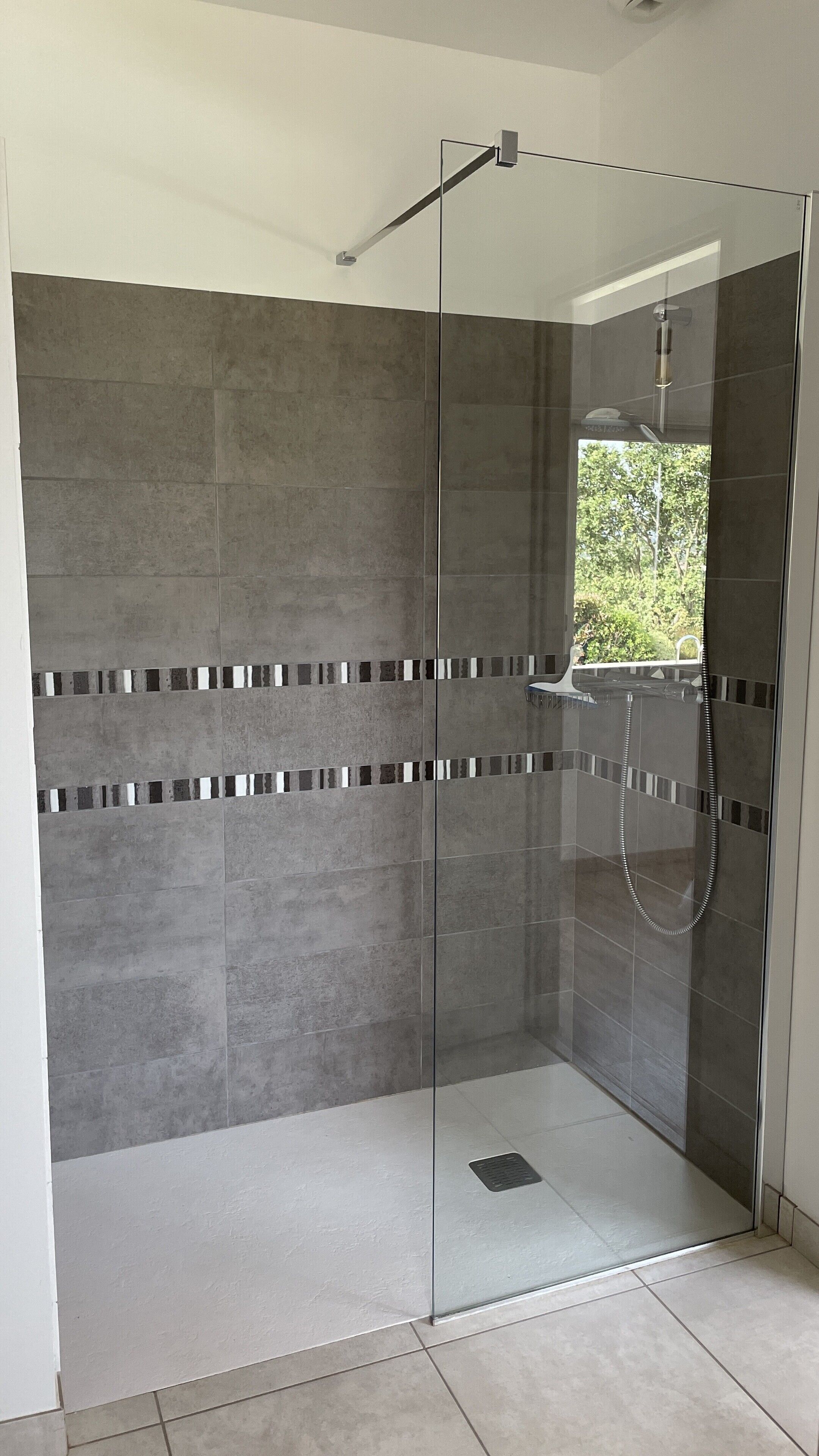 A glass-enclosed shower area with grey tiles and a small window.
