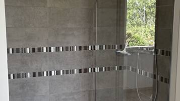 A glass-enclosed shower area with grey tiles and a small window.
