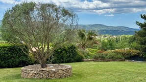 A landscaped garden with a stone planter, lush greenery, and a view of distant hills. - La Maison de Sophie : Luxury Family Villa • Heated Pool • Provence Verte (Garéoult)