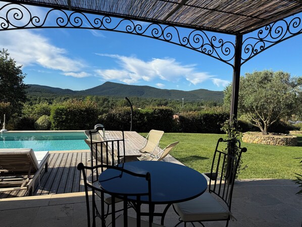 Un área de estar techada al aire libre con piscina, una mesa y sillas.