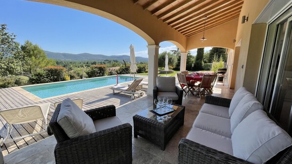 A covered outdoor seating area with a pool, wicker furniture, and a table set for dining.