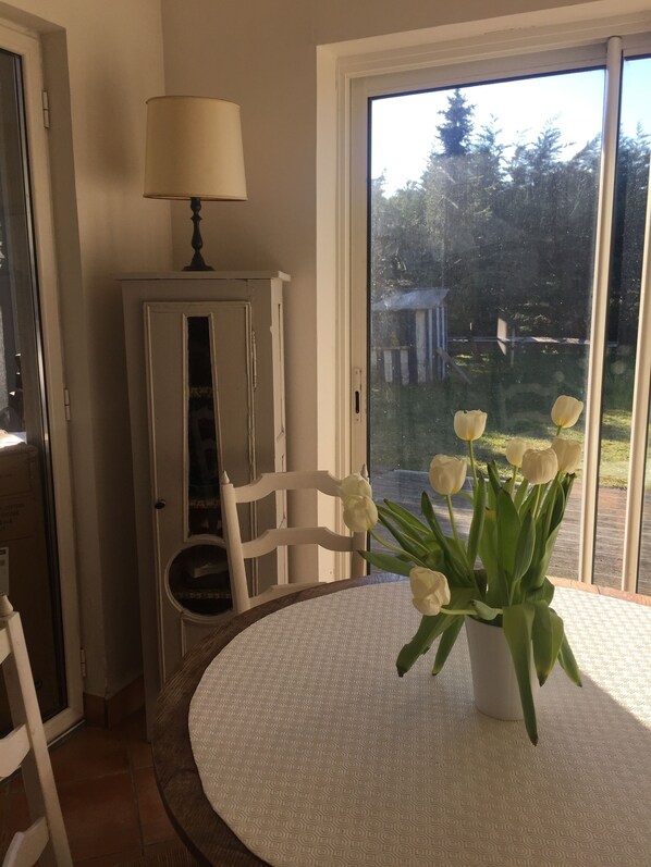A dining area with a round table, chairs, a lamp, and a potted plant with white flowers. - 300 meters from the sea, house on enclosed land not overlooked for 9 people. (Manche)