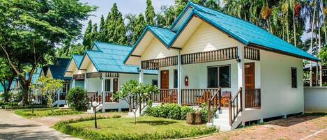 A row of bungalow-style accommodations with blue roofs, surrounded by lush greenery and palm trees.