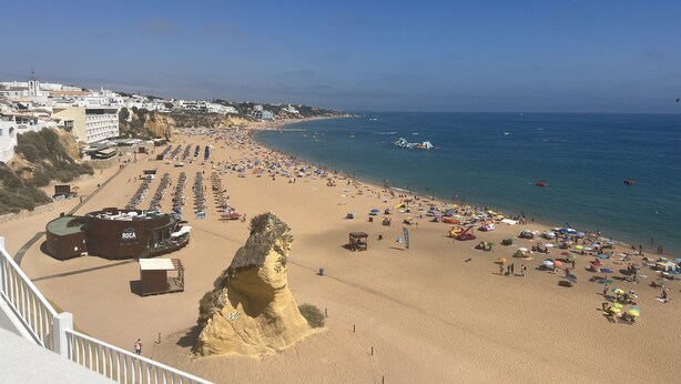 A beach with a rocky outcrop, a row of beach umbrellas, and a clear view of the sea. - OLDTOWN close BEACH  2BR 2BA WIFI++ AC paid PARK
WINTER Underfloor HEATING (Albufeira Praia dos Pescadores)