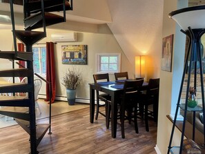 A dining area with a wooden table, chairs, a potted plant, and a spiral staircase.