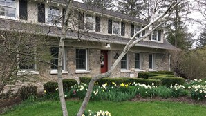 A stone house with a red door, surrounded by a well-maintained garden with daffodils and trimmed hedges. - Genesee Country Inn B&B (Mumford)