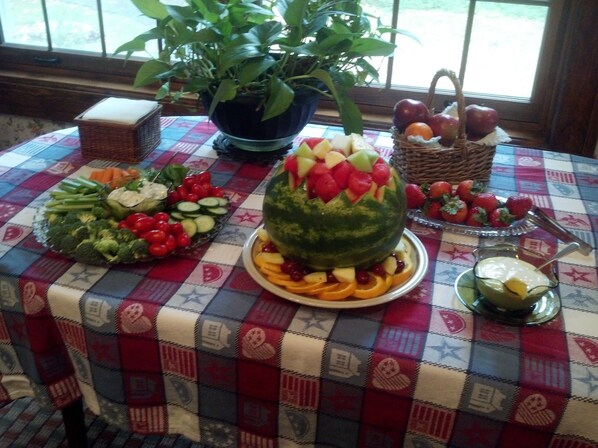 A table with various fruits and vegetables, a watermelon centerpiece, and a potted plant. - Genesee Country Inn B&B (Mumford)