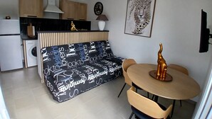 A modern kitchen with wooden cabinets, a built-in oven, and a black countertop. There is a black sofa with white text, a round table with chairs, and a leopard print artwork on the wall. - Gîte-Sassone, gîte with swimming pool, jacuzzi and panoramic sea view. (Ajaccio)