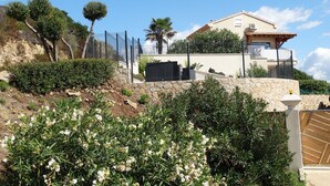 A house with a stone retaining wall, a fenced garden, and a clear blue sky. - Gîte-Sassone, gîte with swimming pool, jacuzzi and panoramic sea view. (Ajaccio)