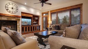 A living room with a fireplace, a large clock, and a television.