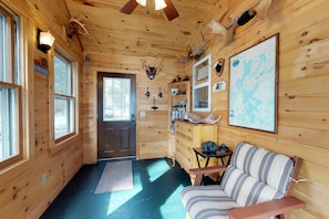 Relax in a cozy cabin-style room with a central seating area, wooden door, and a bookshelf filled with books.