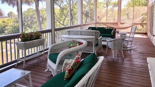 A covered porch with wicker furniture, a hammock, and a view of trees and sky.