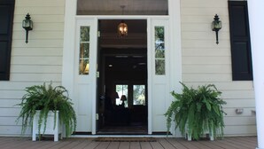A white building with a porch, steps, and two potted plants.
