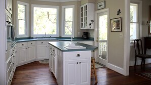 A kitchen with white cabinets, a large island, and a view of trees through the windows.