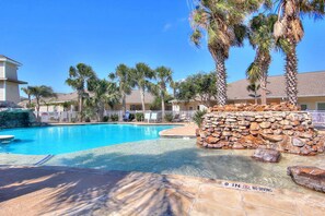 A clear blue pool with a '9 IN' no diving sign, surrounded by palm trees and a stone wall. - Welcoming condo with W/D & pool - near the beach (Corpus Christi)