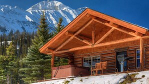 A log cabin with a wooden exterior, a covered porch, and a hot tub.