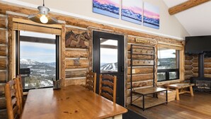 A rustic log cabin interior with a wooden dining table, chairs, a bench, and a fireplace.