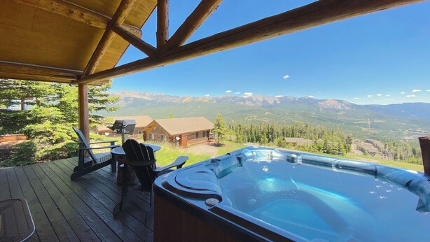 A wooden deck with a hot tub and chairs, overlooking a mountainous landscape.