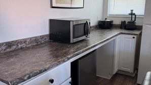 Una cocina compacta con microondas, lavavajillas y una ventana con persianas.