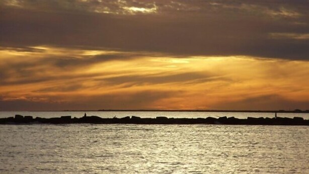 Un atardecer sobre un cuerpo de agua con el silueta difusa de la orilla al fondo.