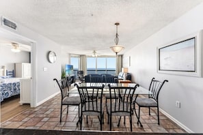 A dining area with a glass table, black chairs, a ceiling fan, and a view of the ocean.